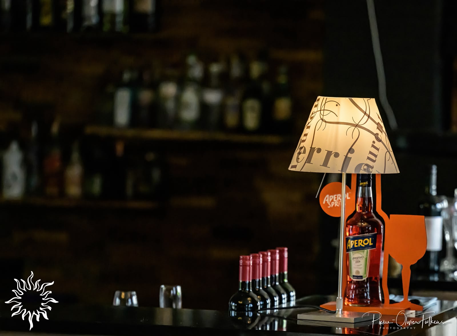 Photo d'une bouteille d'Aaperol posée sur le coin du bar avec une petite lampe de chevet à côté